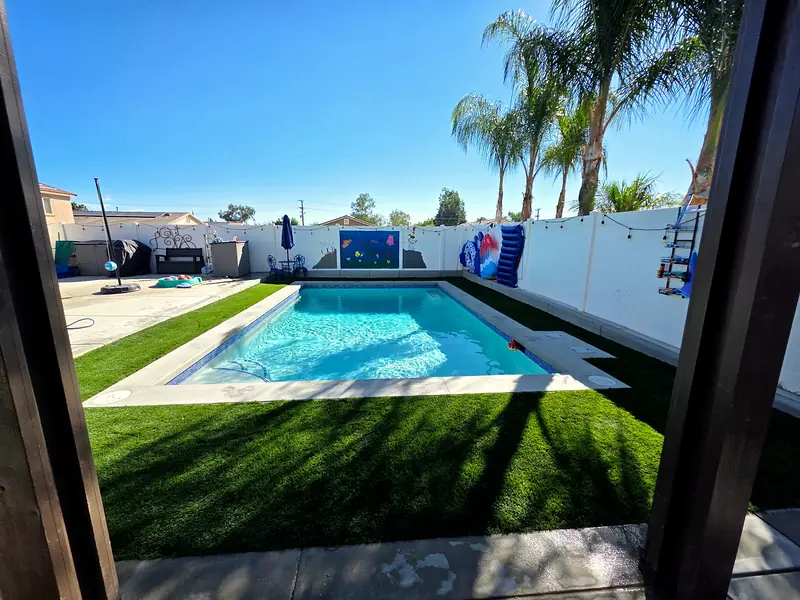 The finished pool and turf yard framed by pergola posts, with palms beyond
